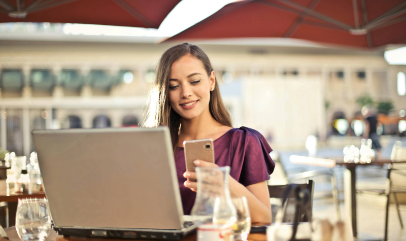Zadovoljna žena koristi laptop i mobitel tijekom online kupnje vitamina – VitaYummy blog