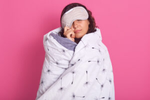 Žena s maskom za spavanje zamotana u dekicu – simbolizira nesanicu i umor prije korištenja dodatka za san VitaYummy Sleep Support